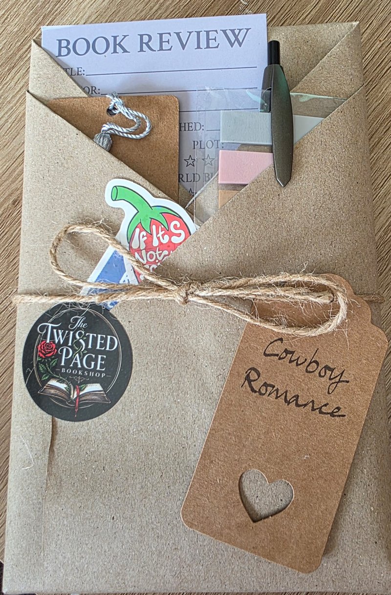 Blind Date with a Book, Cowboy Romance pick — a kraft-paper wrapped parcel tied with twine, with a heart-cutout "Cowboy Romance" gift tag